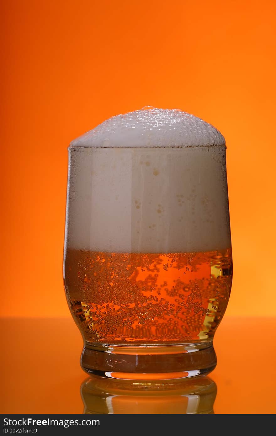 Glass of beer with froth over orange background