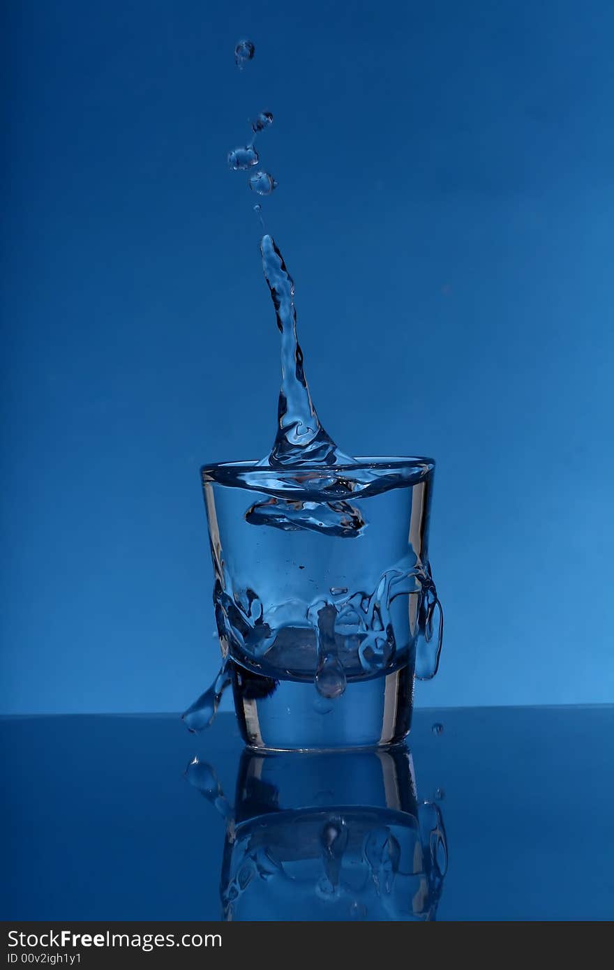 Glass with splashing water over  blue