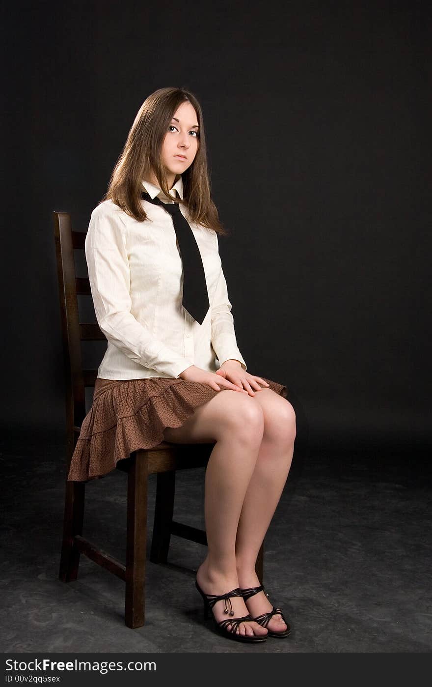 The brunette girl on the stool in a white shirt and black tie