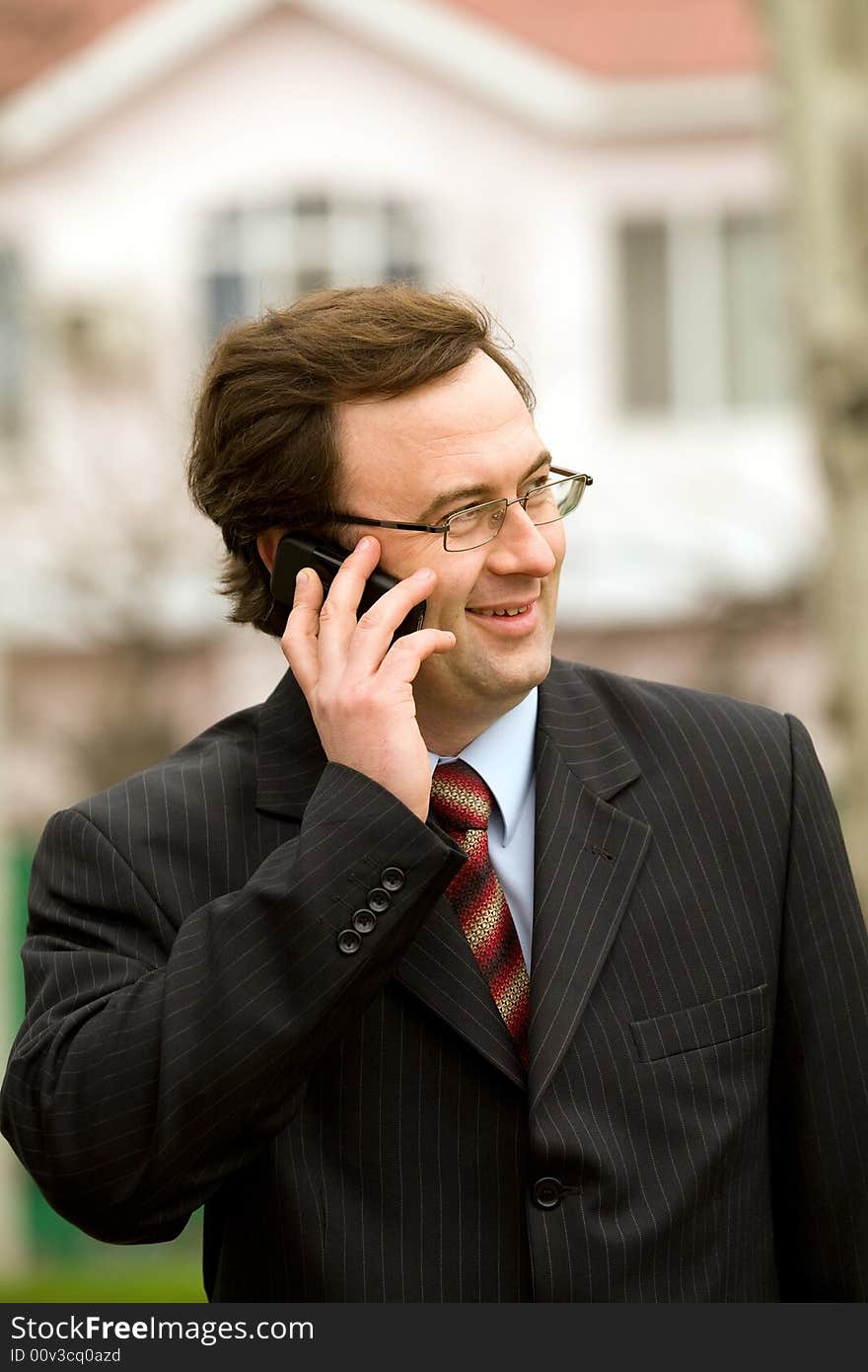 Businessman talking by mobile phone over blurred house background. Businessman talking by mobile phone over blurred house background