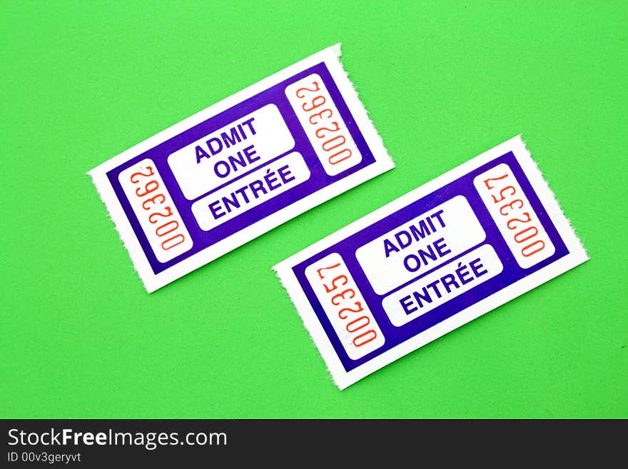 A pair of blue admit one tickets over a green surface