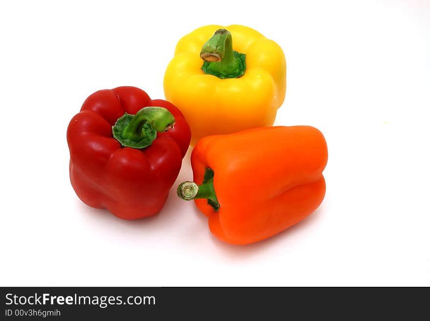 Fresh orange, yellow and red bell peppers over a white surface