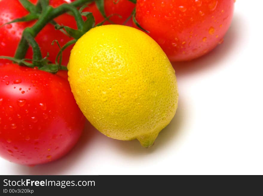 The perfect juicy tomatoes and lemon covered by drops of water, on a green branch. Isolation on white. Shallow DOF.