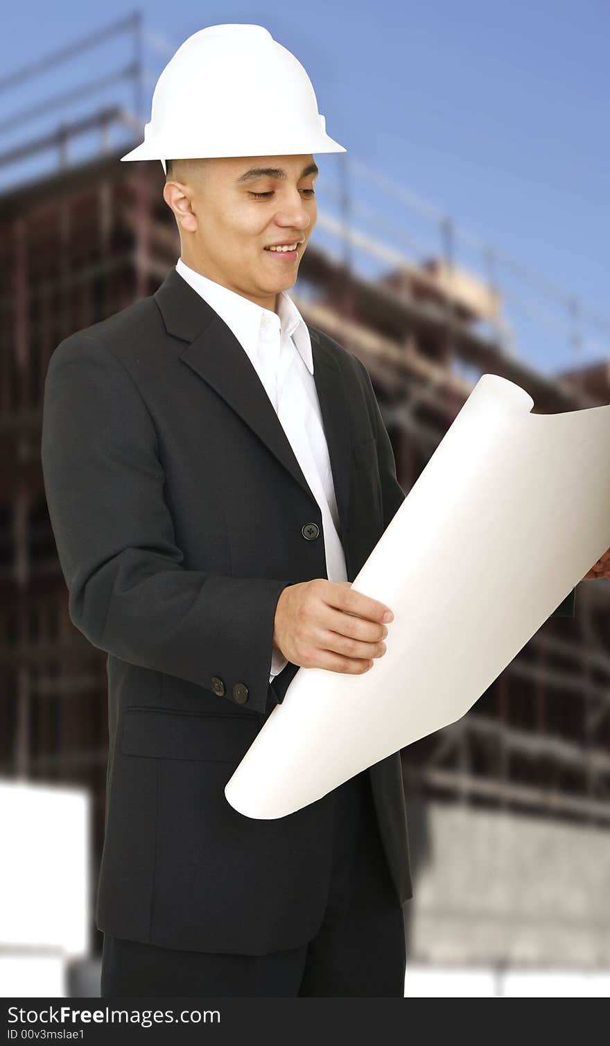 A man wearing hard hat and smiling looking at his floor plan with building under construction behind him. A man wearing hard hat and smiling looking at his floor plan with building under construction behind him