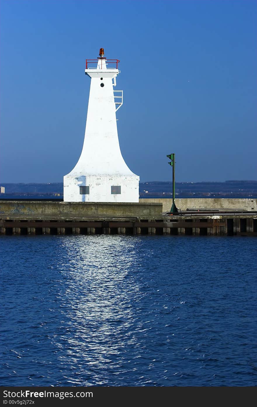 White lighthouse on a pier against a blue sky.