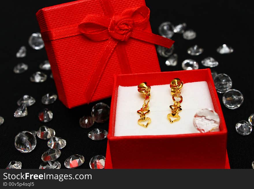 A pair golden earrings in small red box surrounded with crystals.