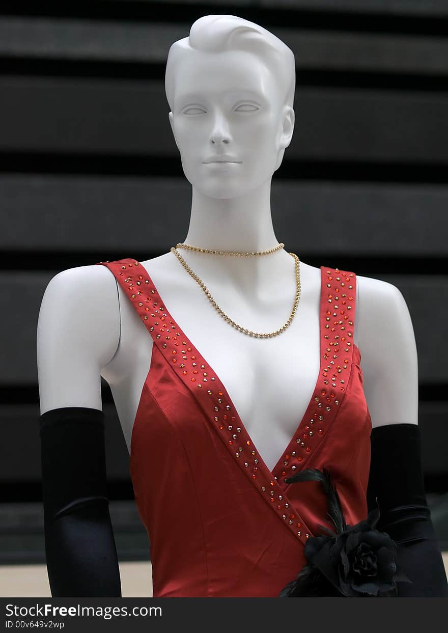 Mannequin dressed in a gown with deep plunging beaded neckline, a black rose ornament, and long velvet gloves, against a black textured wall. Mannequin dressed in a gown with deep plunging beaded neckline, a black rose ornament, and long velvet gloves, against a black textured wall