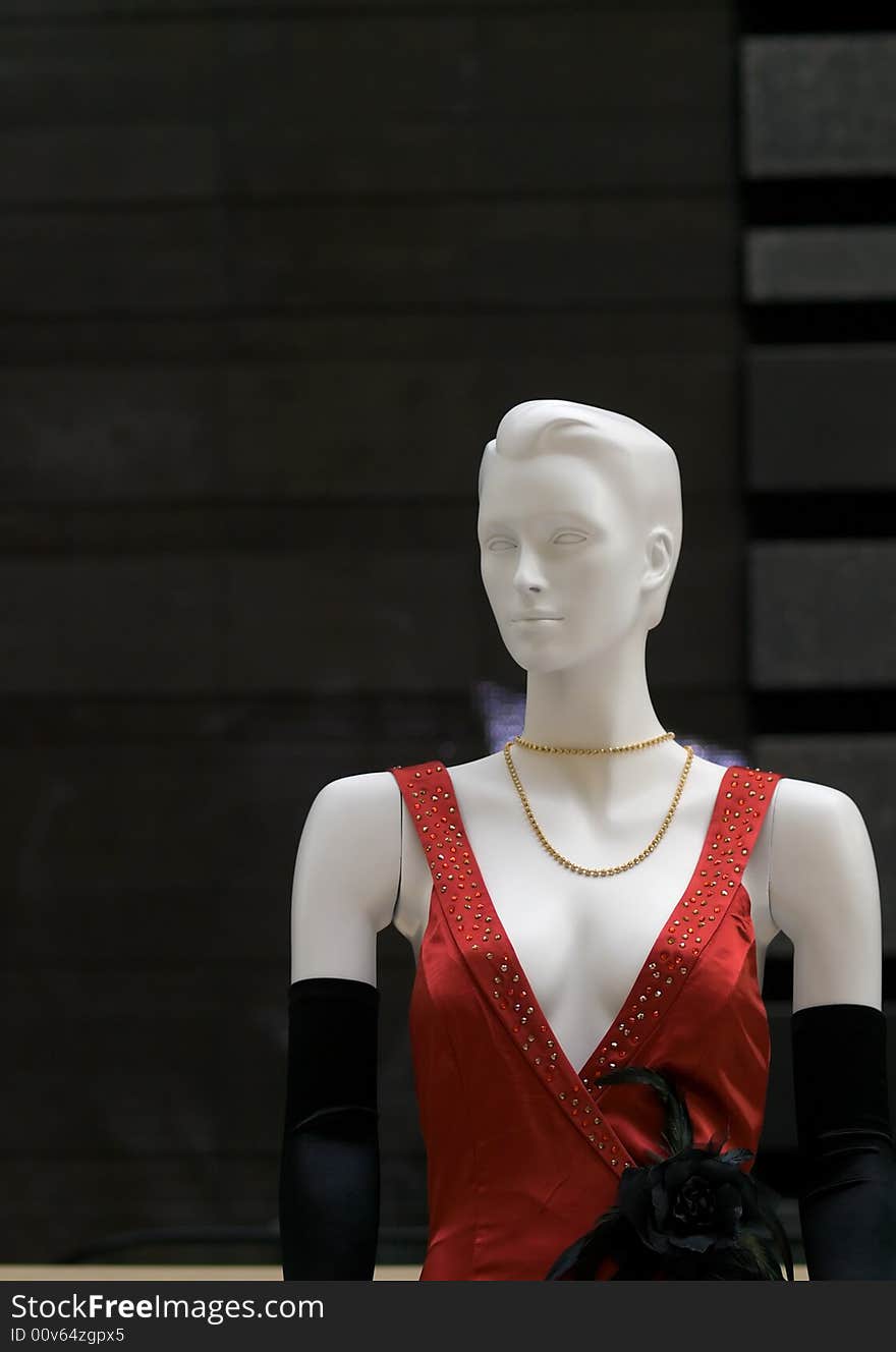 Mannequin dressed in a gown with deep plunging beaded neckline, a black rose ornament, and long velvet gloves, against a textured wall of various shades of black. Mannequin dressed in a gown with deep plunging beaded neckline, a black rose ornament, and long velvet gloves, against a textured wall of various shades of black