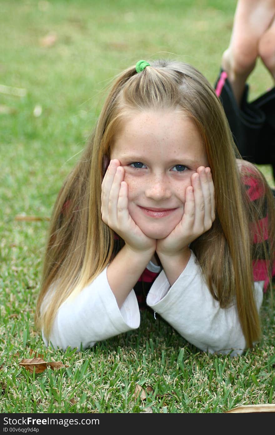 A white caucasian girl lying on the grass with her head in her hands. A white caucasian girl lying on the grass with her head in her hands