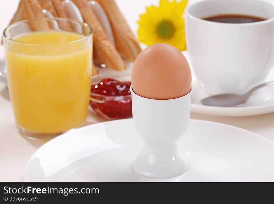 A boiled egg with orange juice, coffee, toast and jam. A yellow flower in the background. A boiled egg with orange juice, coffee, toast and jam. A yellow flower in the background.