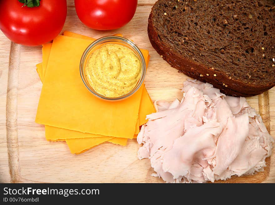 Makings of a turkey sandwich includeing dark german wheat, sliced turkey, tomatoe, spicey mustard, cheddar cheese. Makings of a turkey sandwich includeing dark german wheat, sliced turkey, tomatoe, spicey mustard, cheddar cheese.