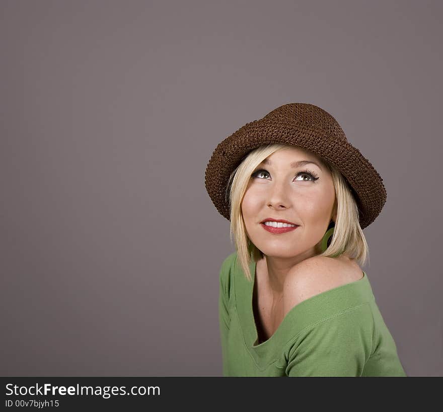 A blonde in a green blouse and a brown hat smiling and looking up. A blonde in a green blouse and a brown hat smiling and looking up