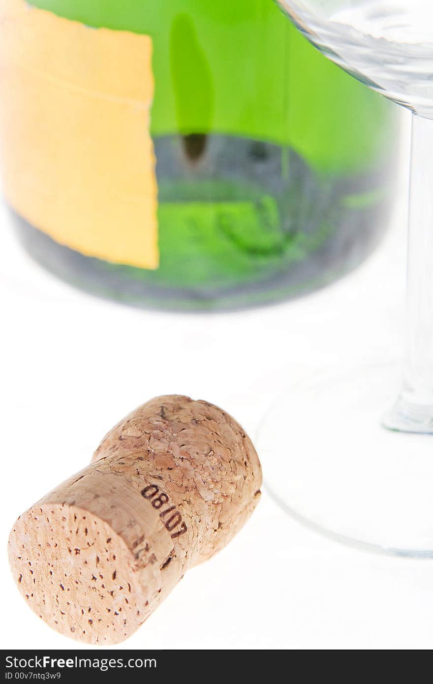 The bottle cork lays near to a bottle and a glass. The bottle cork lays near to a bottle and a glass