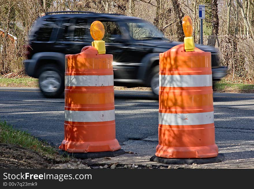 Highway warning cones on a road with a car in the background. Highway warning cones on a road with a car in the background.