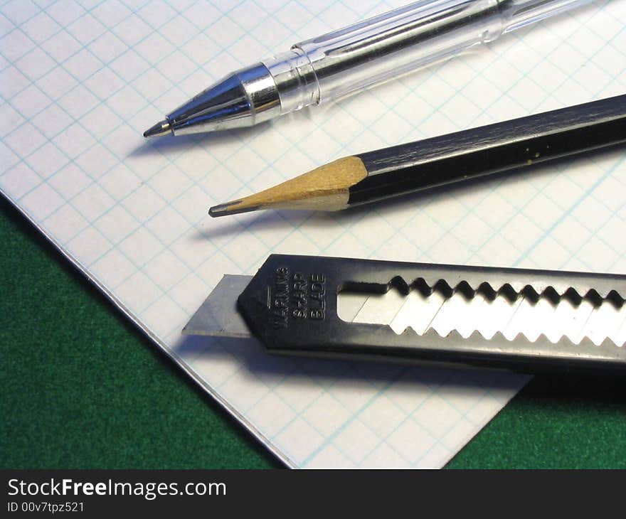 The handle of office, pencil and knife of black color lay on прописи in a cage. The handle of office, pencil and knife of black color lay on прописи in a cage.