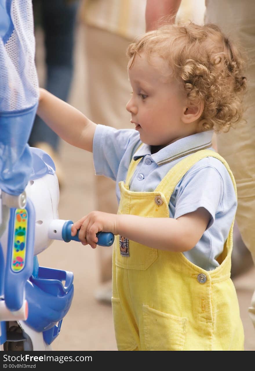 The small curly boy in a yellow overalls walks in city park. The small curly boy in a yellow overalls walks in city park