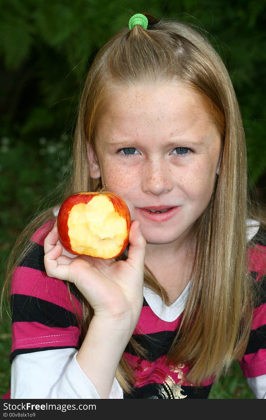 A white caucasian girl child chewing and showing a half eaten apple. A white caucasian girl child chewing and showing a half eaten apple