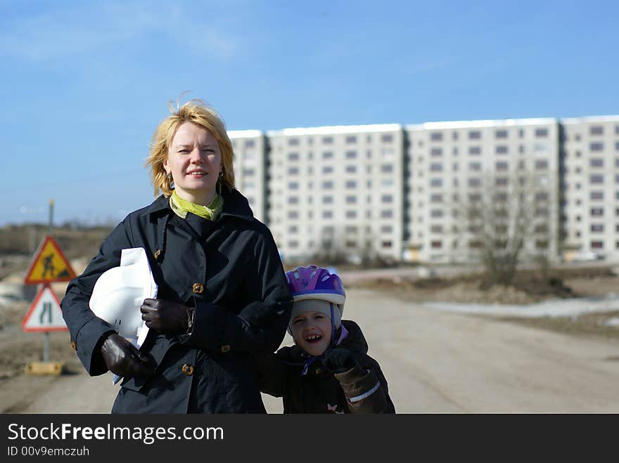 Women architect and her daughter with blueprints and hard hat at site