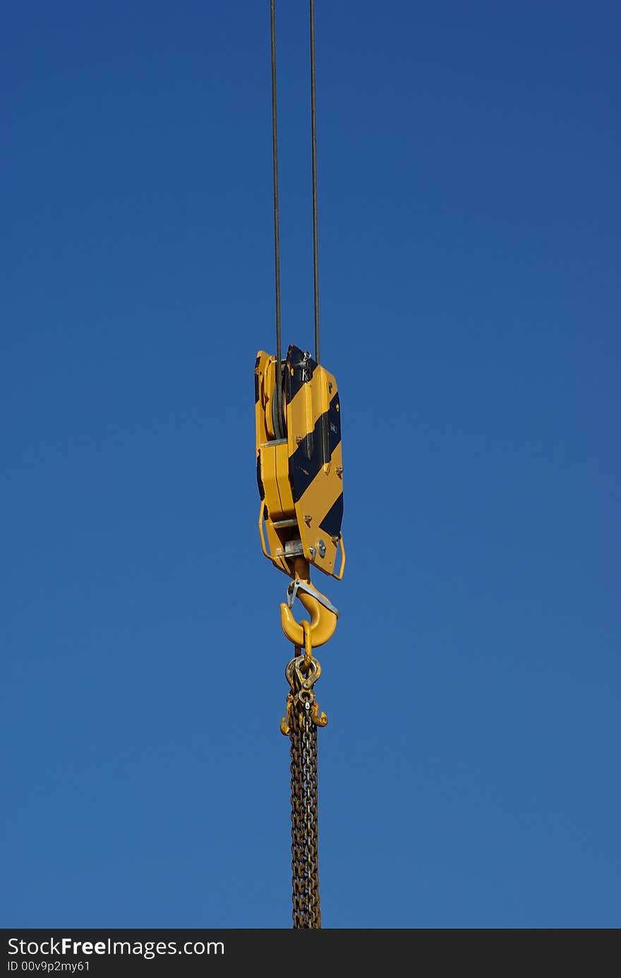 A closeup of crane hook against clear blue sky.