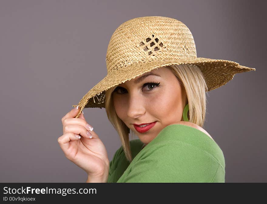 A blonde in green blouse and straw hat pulling the brim over her eyes. A blonde in green blouse and straw hat pulling the brim over her eyes