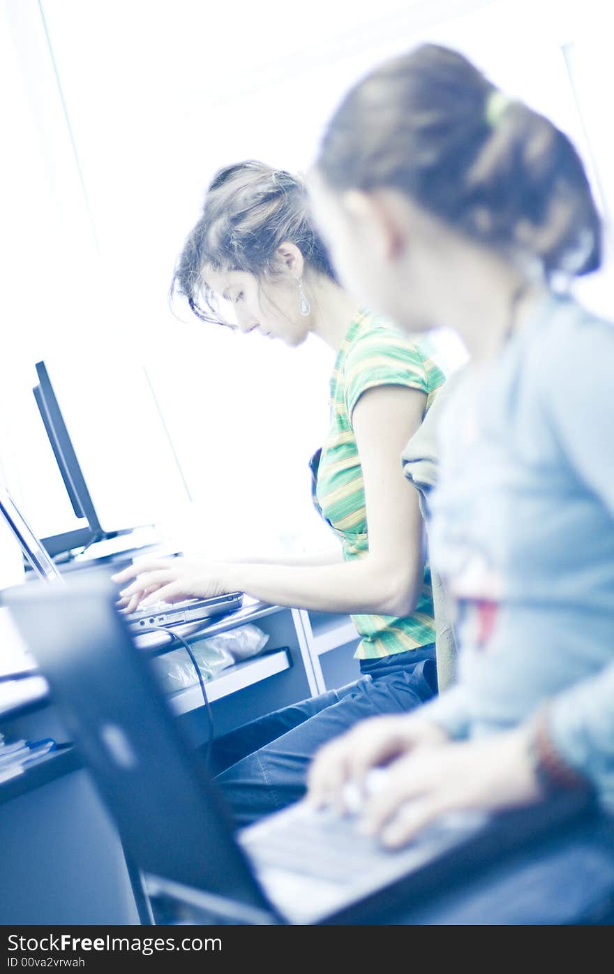 Beautiful girl with computer in office space. Young teen girl learning computers in foreground. Beautiful girl with computer in office space. Young teen girl learning computers in foreground.