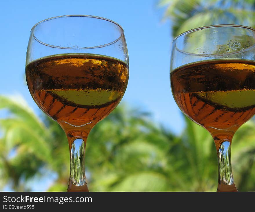 Two beer glasses with sky and palm trees behind