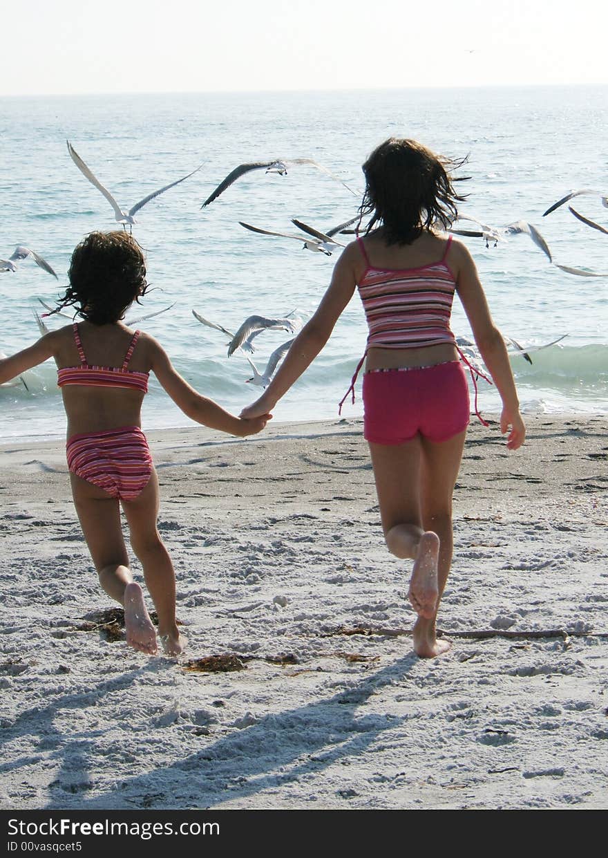 Two young girls chasing birds on the beach