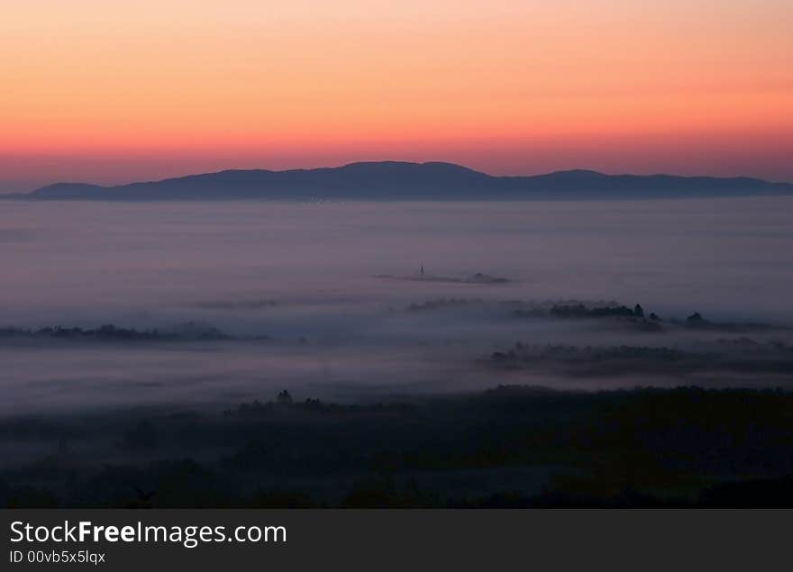 High-wide angle shot of a beautiful dusk scene over the countryside covered in mist. Bela Krajina. Slovenia. High-wide angle shot of a beautiful dusk scene over the countryside covered in mist. Bela Krajina. Slovenia