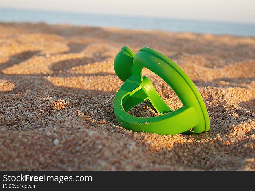 Part of toy is laying on sand during sunset. Part of toy is laying on sand during sunset