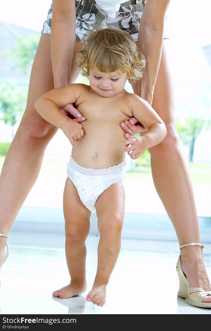 High key portrait of nice baby walking between  mama’s legs. High key portrait of nice baby walking between  mama’s legs