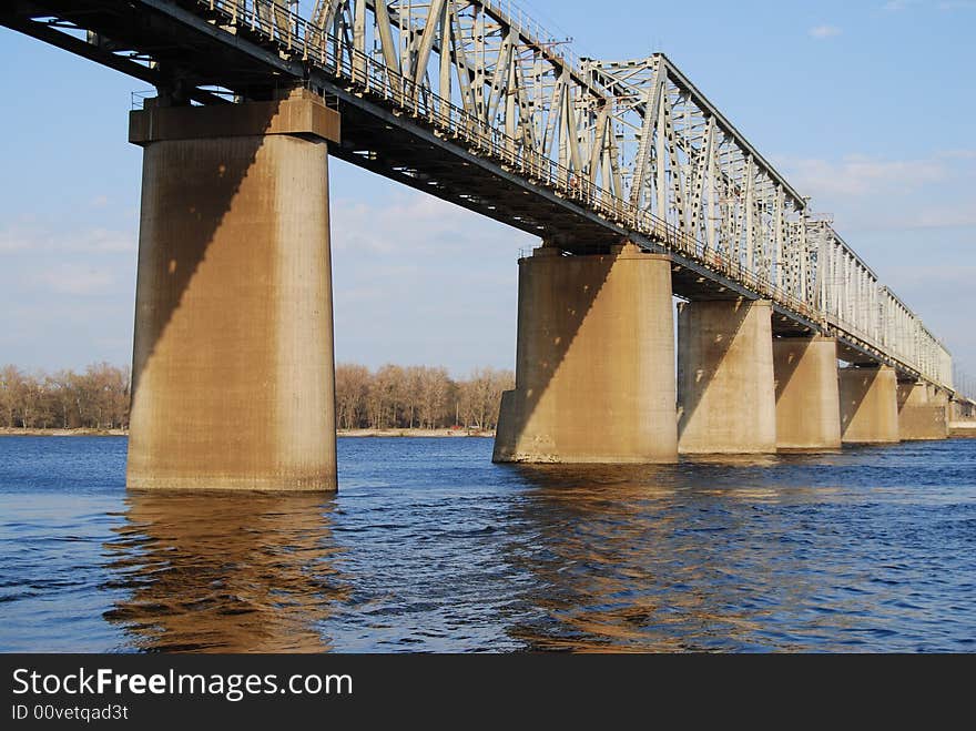 Train bridge over wide river in sunny day with supports mirroring in wavy water. Train bridge over wide river in sunny day with supports mirroring in wavy water