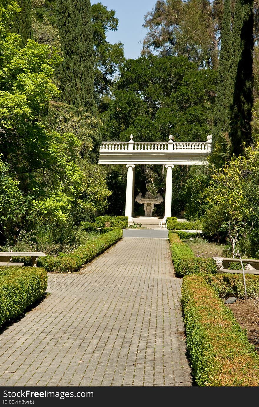 Empty footpath perspective in blooming garden with classic pavilion