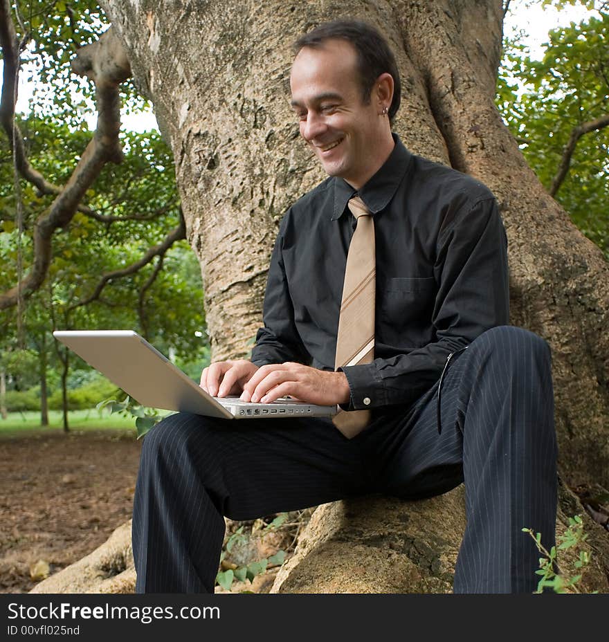 A businessman sitting on giant tree's roots using a laptop. A businessman sitting on giant tree's roots using a laptop.