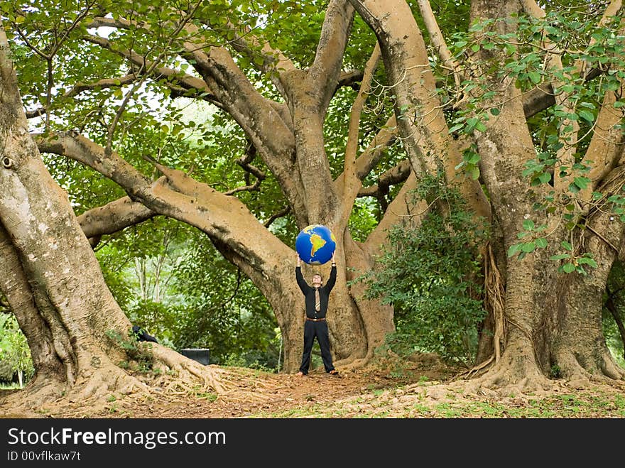 Wide angle shot of a Latin American businessman standing in a grove of trees with an inflatable globe held above his head. Wide angle shot of a Latin American businessman standing in a grove of trees with an inflatable globe held above his head