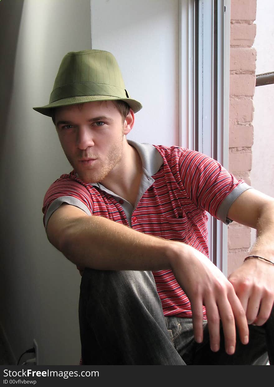 A young man sitting next to a windowsill, with a provocative look on his face. A young man sitting next to a windowsill, with a provocative look on his face.