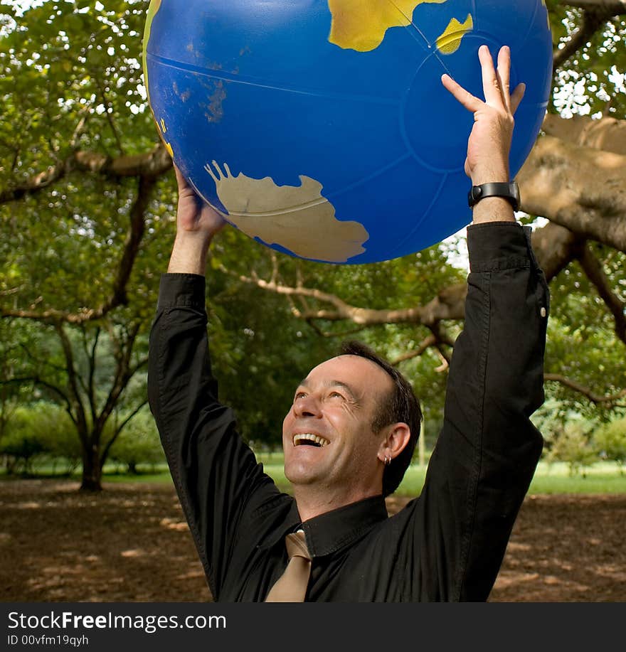 Latin American businessman standing in a grove of trees with an inflatable globe held above his head. Latin American businessman standing in a grove of trees with an inflatable globe held above his head