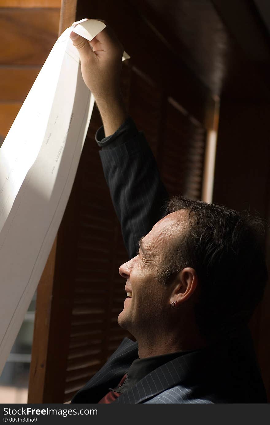 A business man smiling while reading long printout. A business man smiling while reading long printout.