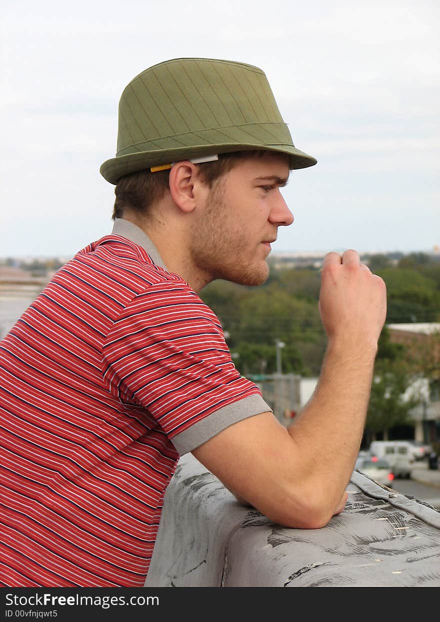 A man on a roof top wearing a green hat with a cigarette behind his ear. A man on a roof top wearing a green hat with a cigarette behind his ear.