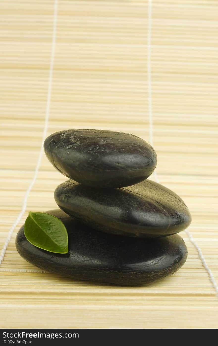 Balanced black zen pebbles and a young green leaf on bamboo mat. Alternative therapy and new life symbol. Balanced black zen pebbles and a young green leaf on bamboo mat. Alternative therapy and new life symbol.