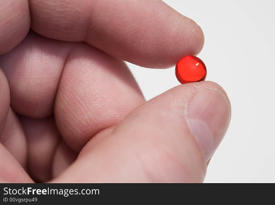 Fingers hold a red pill. Close-up, shallow depth of field. Fingers hold a red pill. Close-up, shallow depth of field.