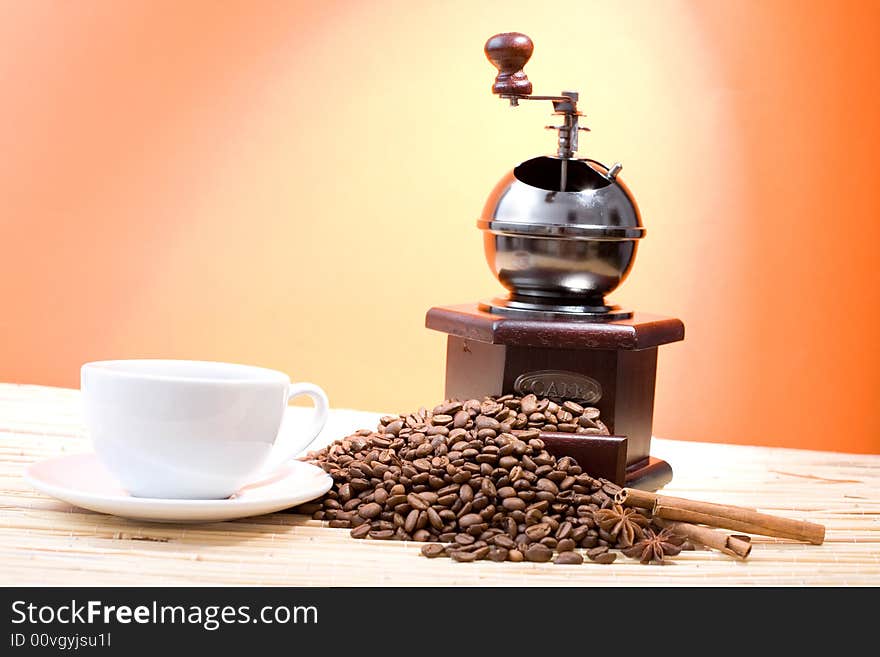 Grinder, cup of coffee, coffee beans and sticks of cinnamon on hot orange background