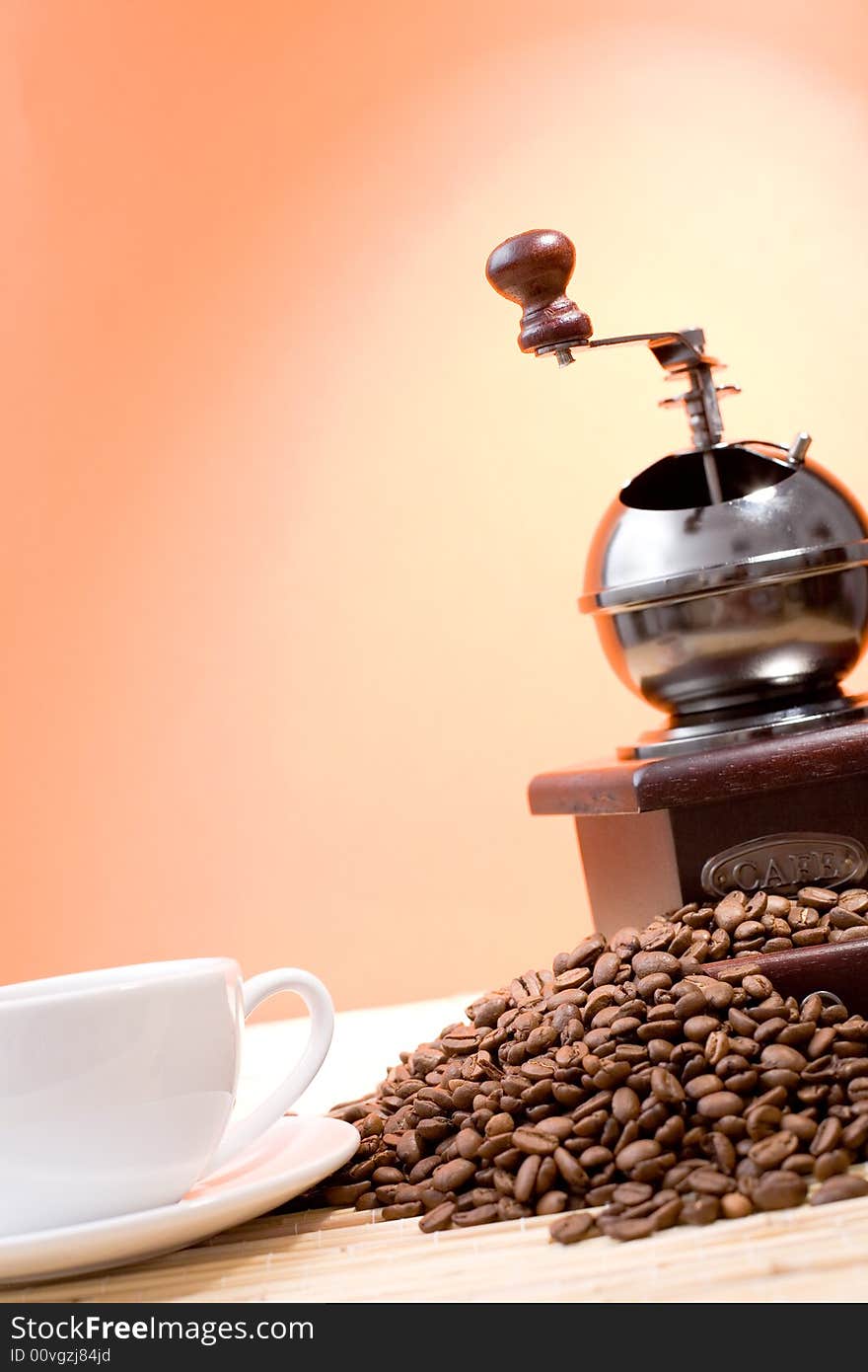 Coffee grinder, cup of coffee, coffee beans and sticks of cinnamon on hot orange background