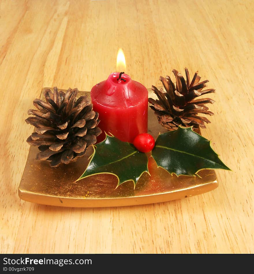 Candle with holly and pine cones on a gold platter as a Christmas theme. Candle with holly and pine cones on a gold platter as a Christmas theme