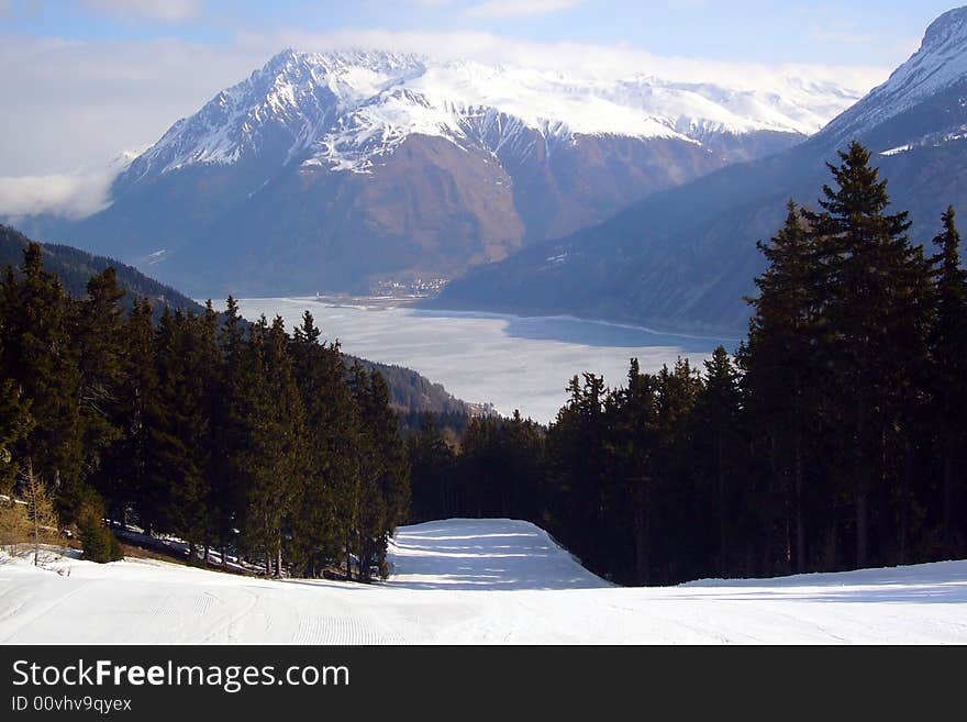 A ski slope with a lake and the mountains as a background.