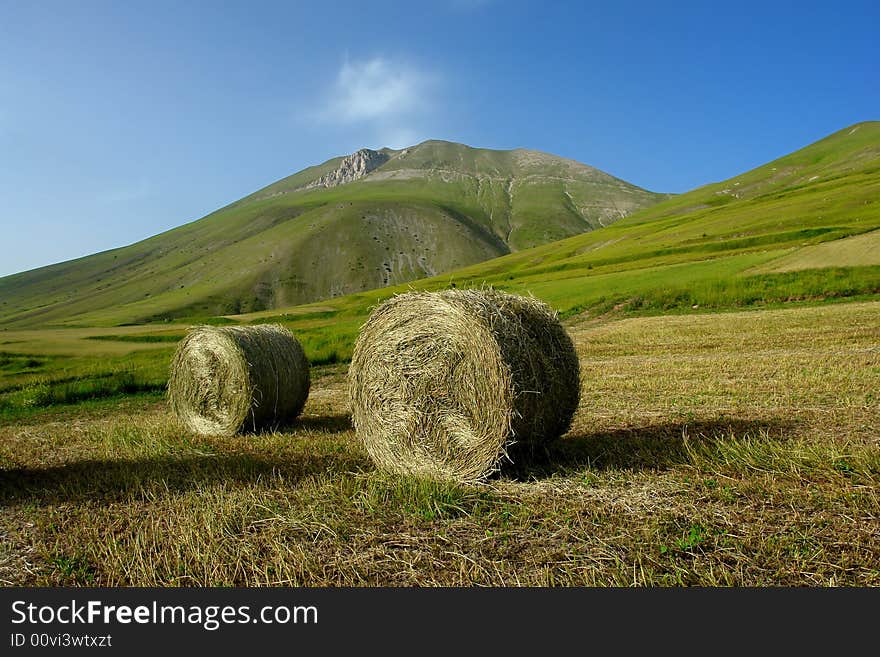 Enormous Hay Balls at the feet of a Mountain. This is a very High Plateau. It's a Summertime afternoon (June) . Enormous Hay Balls at the feet of a Mountain. This is a very High Plateau. It's a Summertime afternoon (June) .