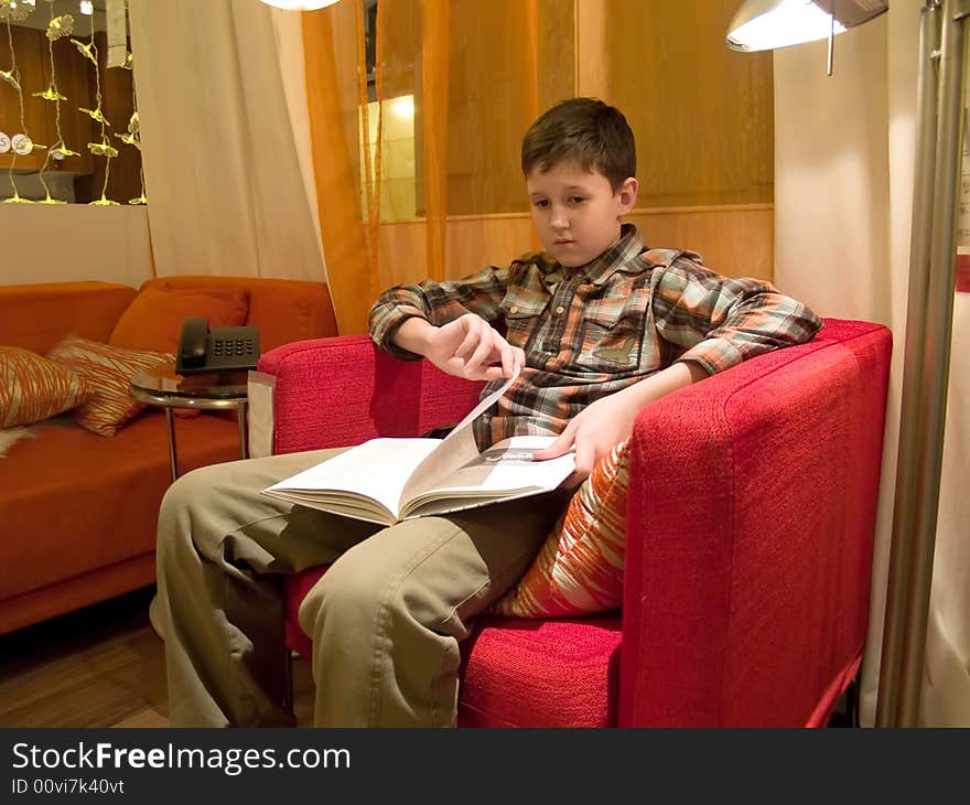 The boy sitting in a red armchair and reading the book. The boy sitting in a red armchair and reading the book