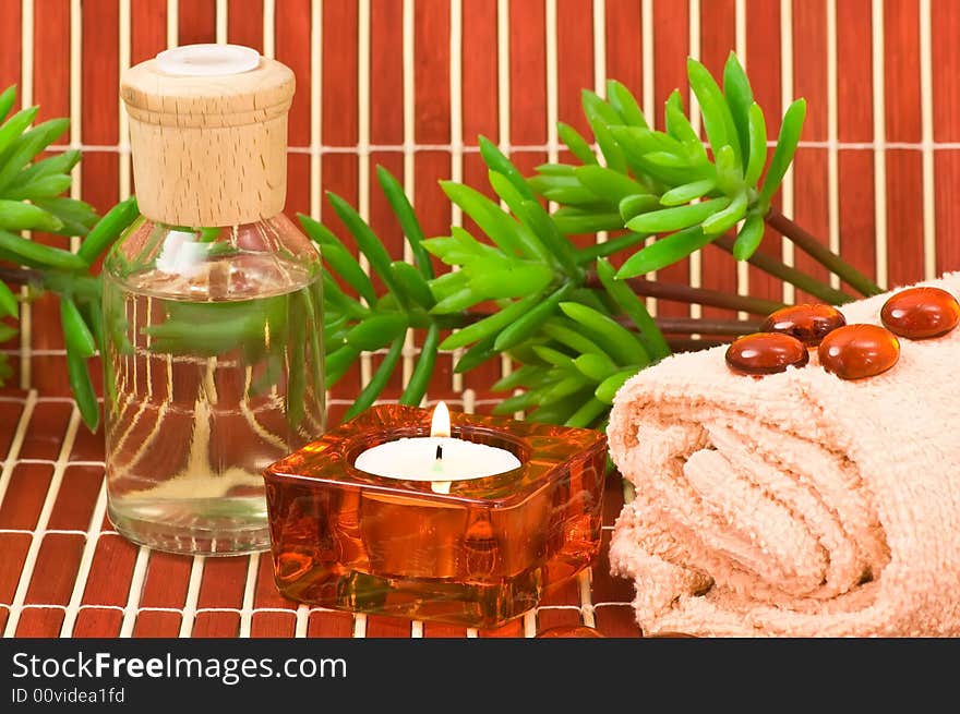 Aromatherapy bottle, glass pebbles, towel, candle and green plants on bamboo. Aromatherapy bottle, glass pebbles, towel, candle and green plants on bamboo