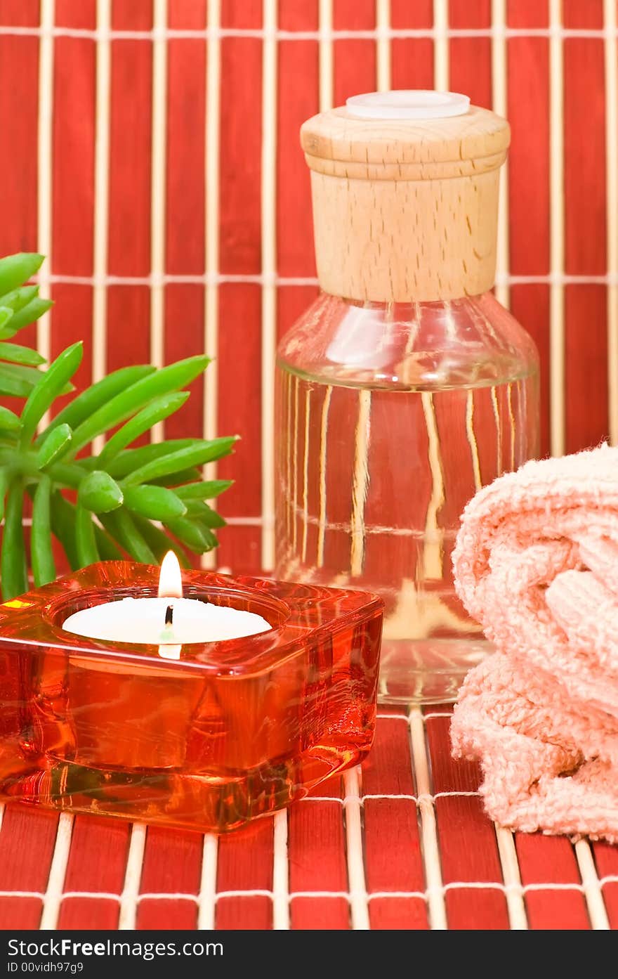 Aromatherapy bottle with towel, candle and green plant on bamboo