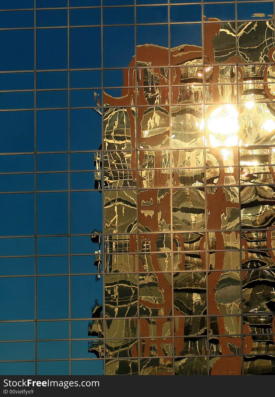 A golden glassed building is reflected in another glassed walled building. A golden glassed building is reflected in another glassed walled building.