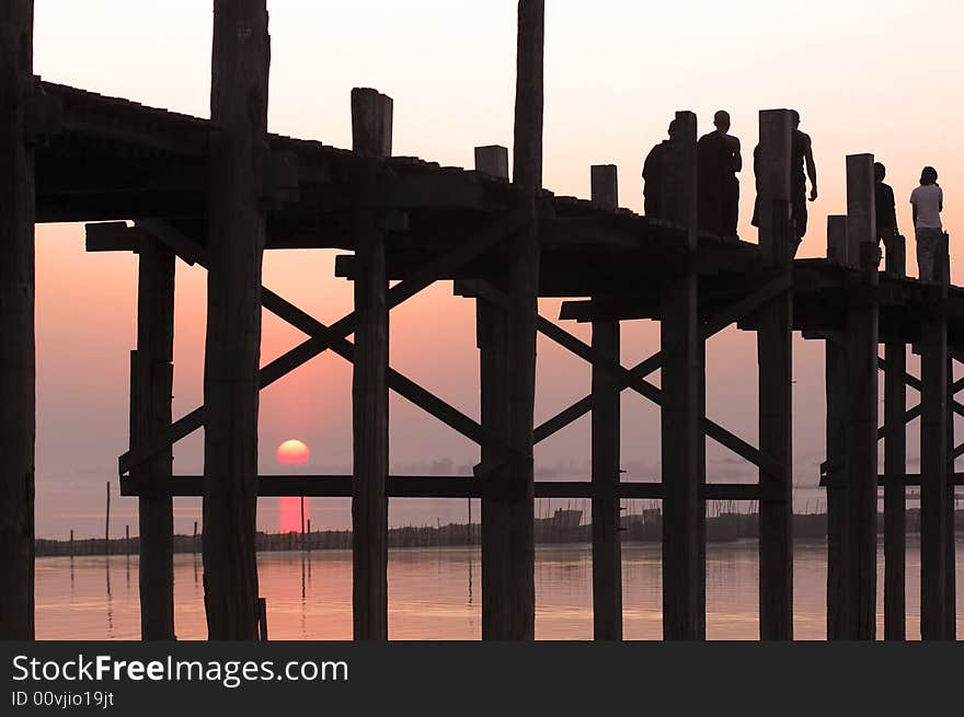 Myanmar, Amarapura, U Bein bridge; stunning sundown from U bein bridge with the shadow of the red dressed buddhist young monks